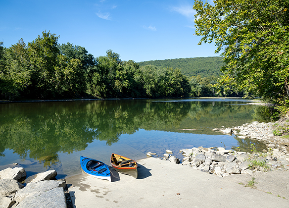 A kayak and a canoe sit at the end of the concrete ramp ready to launch. Boulders line the shore on both sides of the launch.